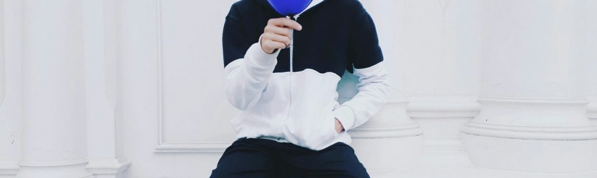 Student sitting with blue ballon in a white room.