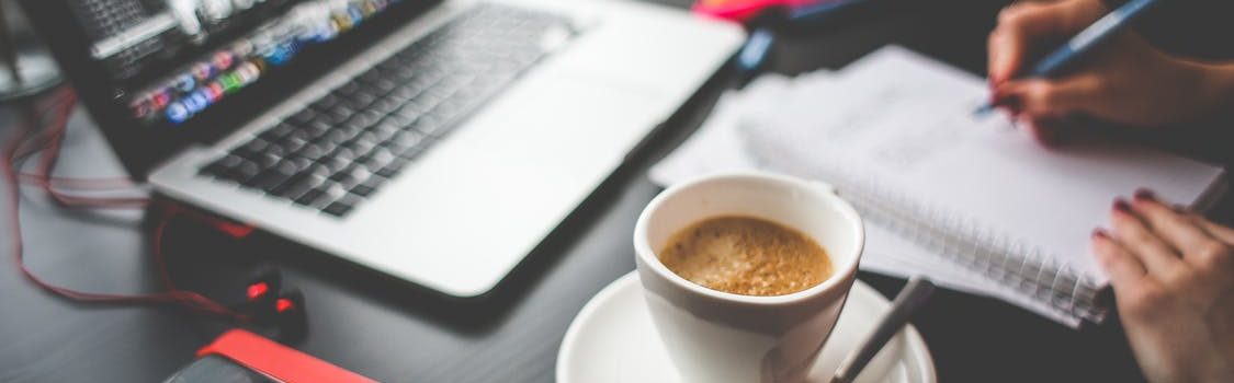 Student writing some notes and watching photos on her laptop in front of her with cup of coffee. Searching for new ideas, ideas of Isaac Asimov can inspire.