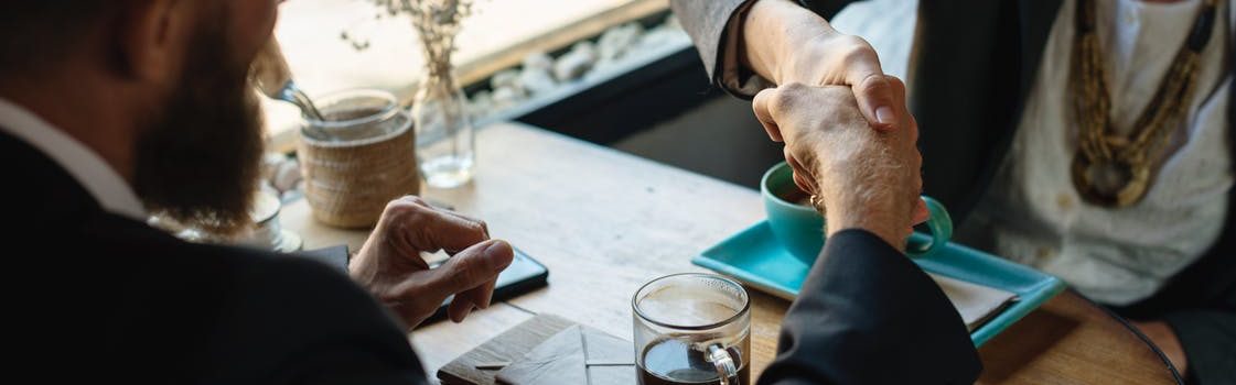 A woman and a man shaking hands one to each other and having a cup of coffee.