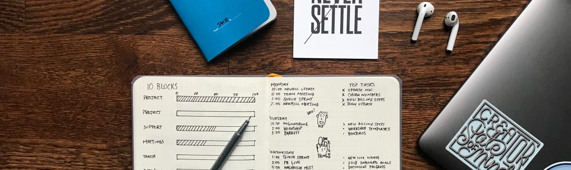 Notes with blue cover and headphones, a pen and a notebook on wooden table.