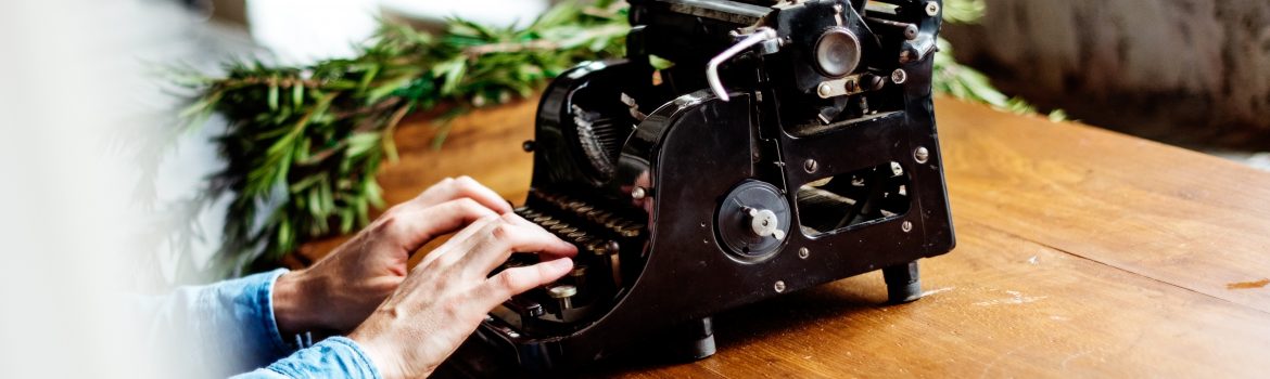 Typing machine and a man typing some text. On the wooden table with green branches.