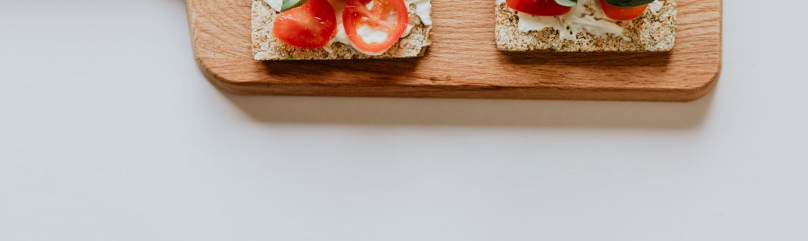 Cutting Board with small loads of bread with tomato and avocado on it and spinach.