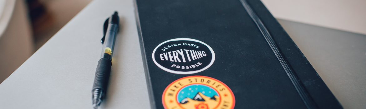 Black notebook with colourful stickers on it with a pen on the table.