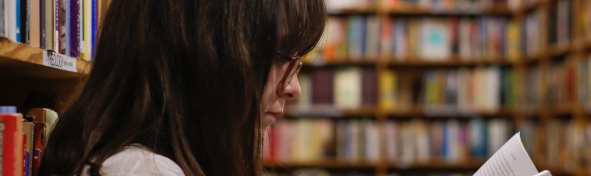 Girl in glasses in the library is sitting and reading a book.