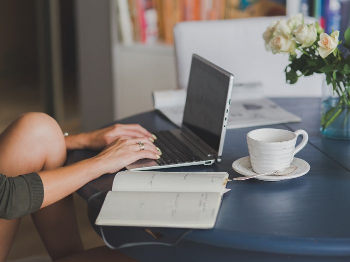 Girl typing something on her notebook with her notes open and a cup of tea on the table